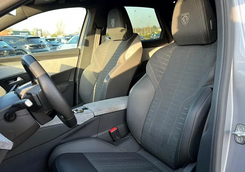Vue intérieure côté conducteur du Peugeot 3008 gris 2025, sièges sport avec logo Peugeot brodé sur appuie-tête.
