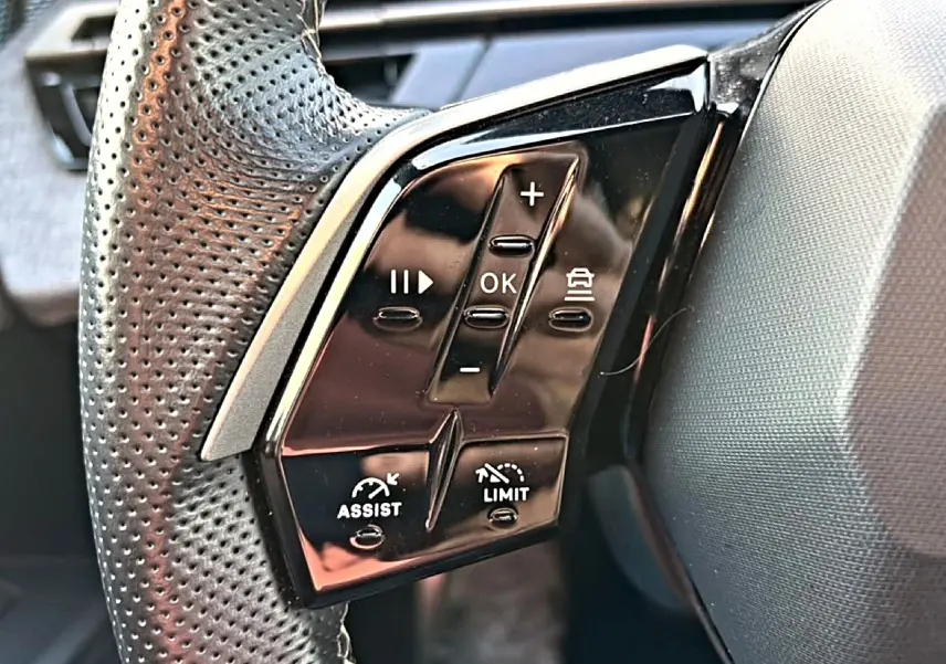 Gros plan sur les commandes noires multifonctions au volant cuir perforé côté gauche du Peugeot 3008 gris 2025.