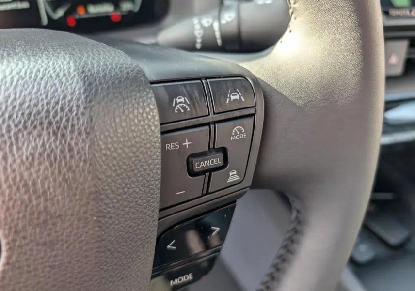 Gros plan sur les commandes de régulateur de vitesse au volant du Toyota C-HR blanc 2024, version hybride.