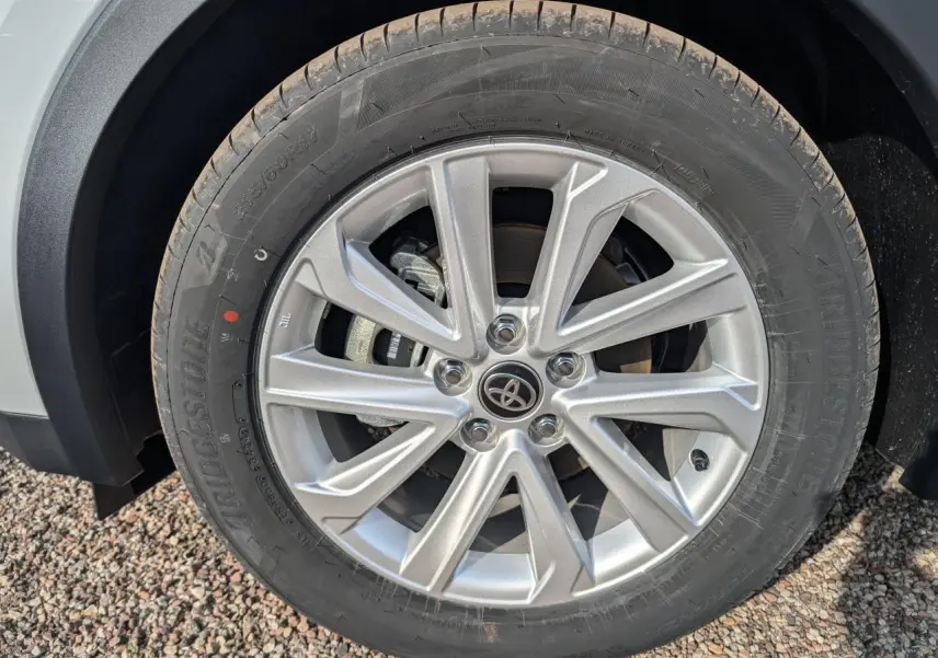 Gros plan sur la roue avant droite d'un Toyota C-HR blanc 2024, avec jante alliage à dix branches et logo Toyota central.