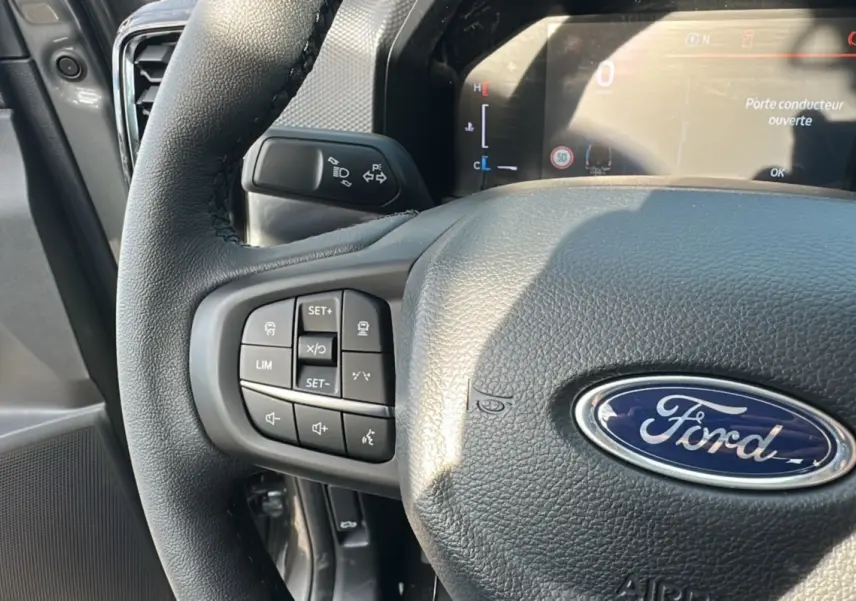 Gros plan sur le volant en cuir noir du Ford Ranger 2025 avec commandes multifonctions et tableau de bord digital.