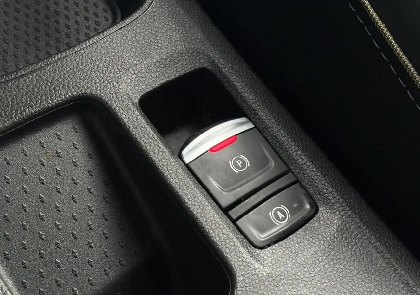 Gros plan sur les commandes du frein de parking électrique et auto-hold dans le console centrale noire du Renault Symbioz bleu Iron.