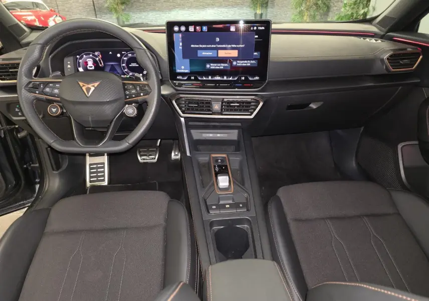 Vue intérieure avant du Cupra Formentor 2025 avec tableau de bord noir, écran tactile central et volant sport à logo cuivre.
