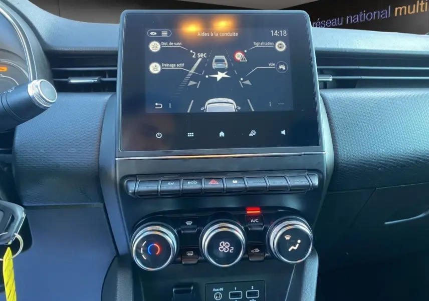 Vue rapprochée du tableau de bord central de la Renault Clio Business E-TECH 140, écran tactile et commandes climatisation visibles.