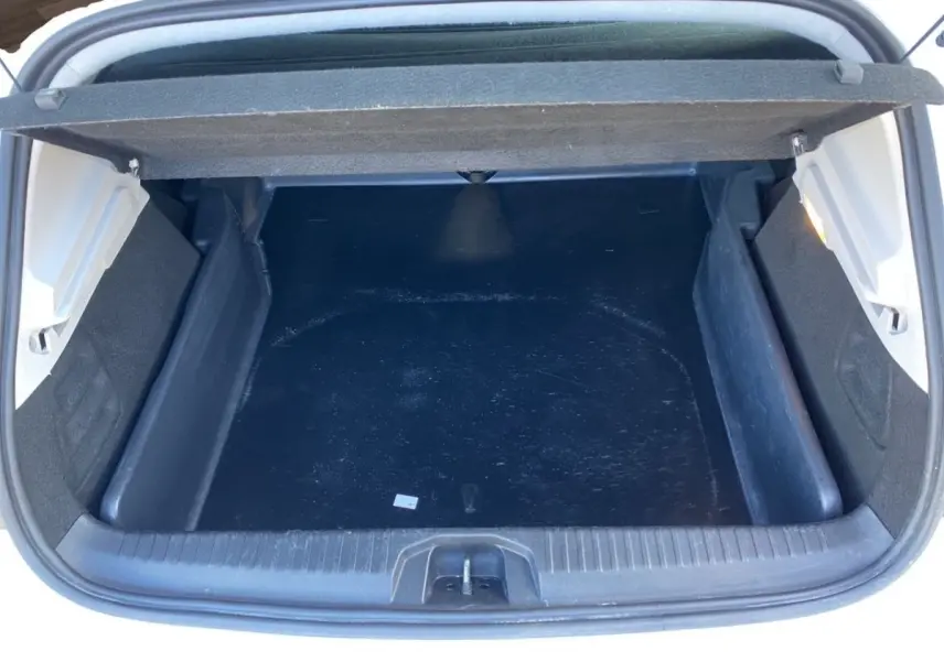 Vue plongeante sur le coffre ouvert d'une Renault Clio blanche, montrant un espace de chargement noir vide.