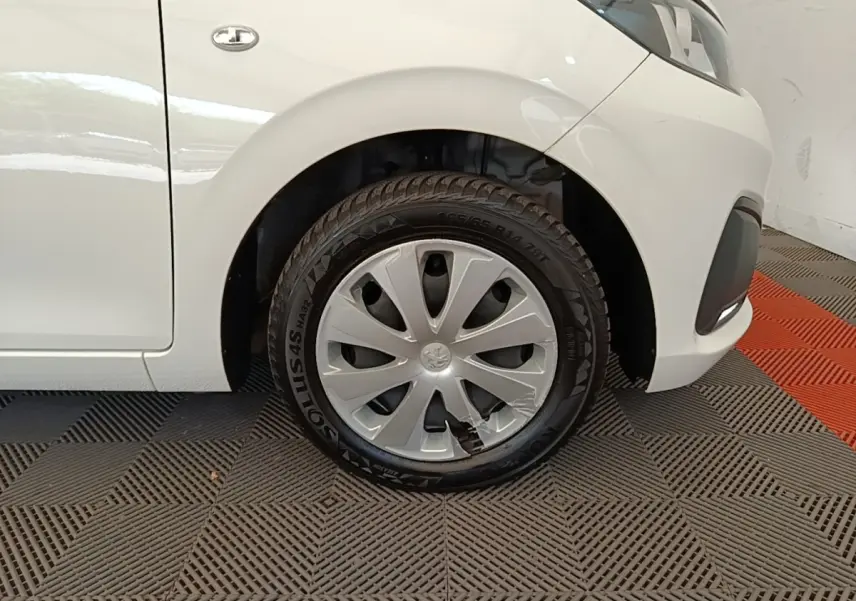 Gros plan sur la roue avant gauche d'une Peugeot 108 blanche, avec enjoliveur abîmé visible sur le pneu.