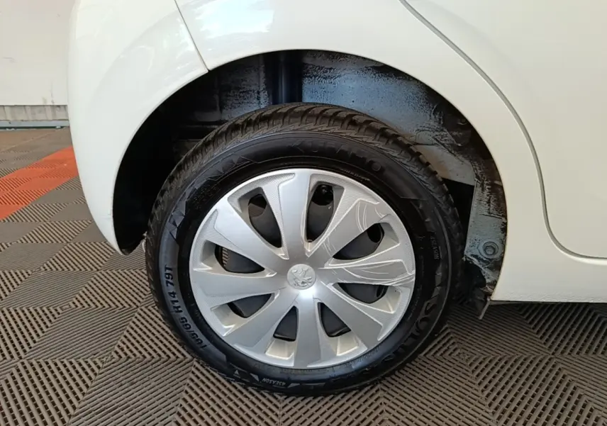 Gros plan sur la roue arrière droite d'une Peugeot 108 blanche, avec enjoliveur argenté et pneu noir visible.