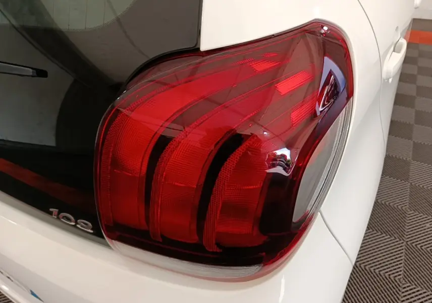 Gros plan sur le feu arrière droit rouge d’une Peugeot 108 blanche, avec une partie de la lunette arrière visible.