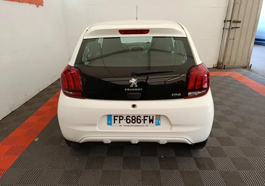 Vue arrière d'une Peugeot 108 blanche, avec lunette arrière noire et feux arrière rouges dans un garage.