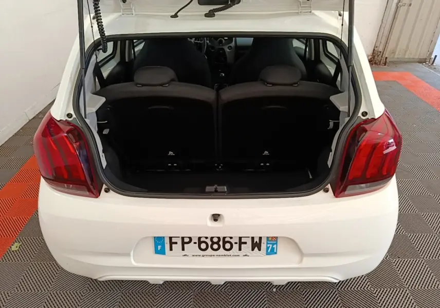 Vue arrière d'une Peugeot 108 blanche avec coffre ouvert, montrant les sièges arrière et les feux rouges.