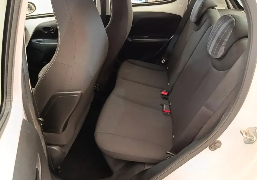 Vue intérieure côté droit sur la banquette arrière noire d'une Peugeot 108 blanche, avec appuie-têtes et ceintures visibles.