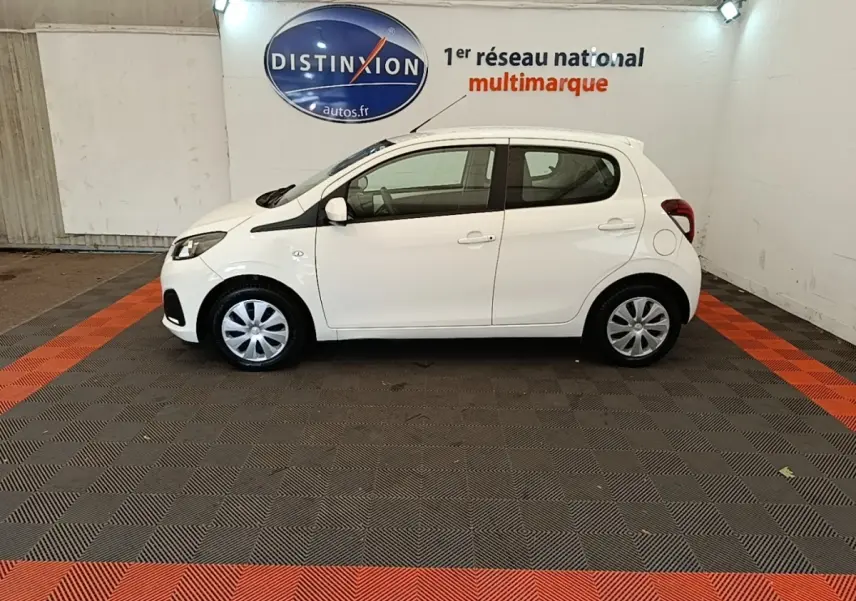 Profil droit d'une Peugeot 108 blanche VTI 72 S&S Active, compacte et citadine, dans un showroom intérieur.