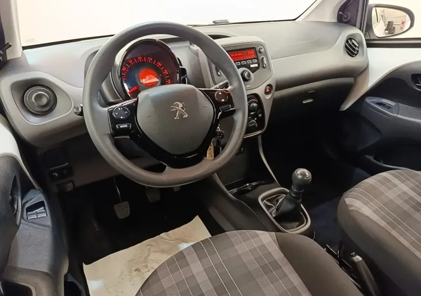 Intérieur de Peugeot 108 blanc, vue côté conducteur sur le volant multifonctions et la console centrale avec boîte manuelle.