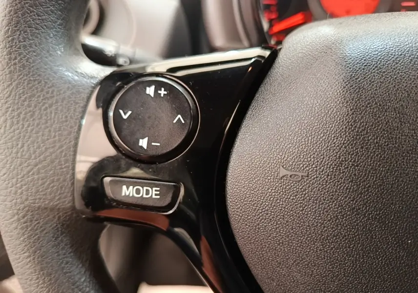 Gros plan sur le volant multifonctions noir de la Peugeot 108 blanc, avec commandes de volume et bouton mode visibles.