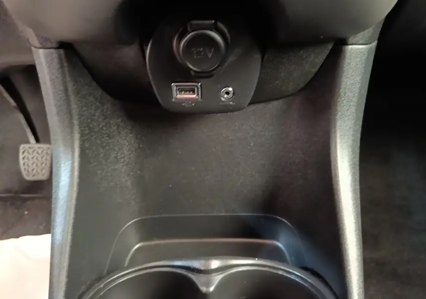 Vue rapprochée de la console centrale noire du Peugeot 108 avec prise 12V, port USB et prise jack.