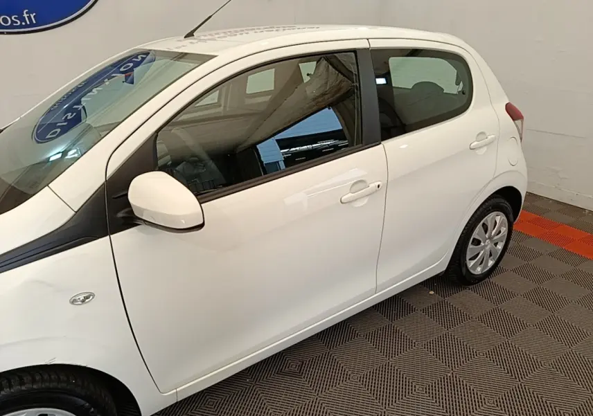 Vue de profil côté gauche d'une Peugeot 108 blanche stationnée en intérieur sur sol à motifs.