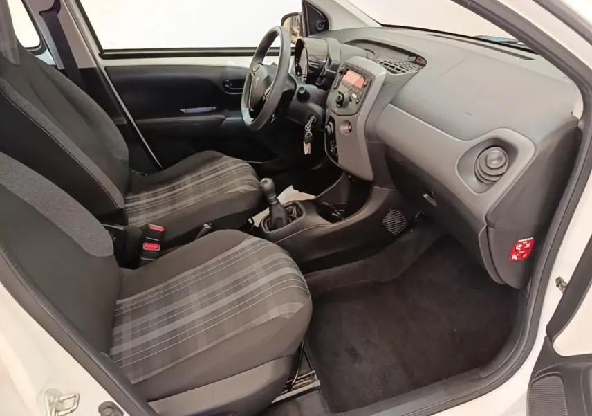 Vue intérieure côté conducteur de la Peugeot 108 blanche, montrant sièges à motifs et tableau de bord compact.