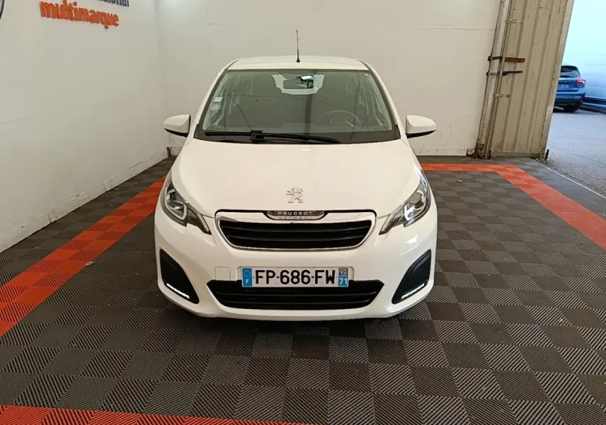 Peugeot 108 blanc vue de face dans un garage avec feux diurnes LED allumés et plaque d'immatriculation visible.