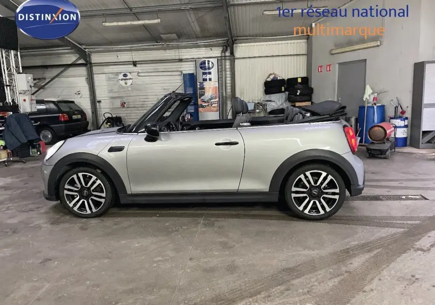 Vue de profil côté gauche d'une MINI Cabriolet F57 2023 Melting Silver Metal avec capote ouverte en intérieur d'atelier.