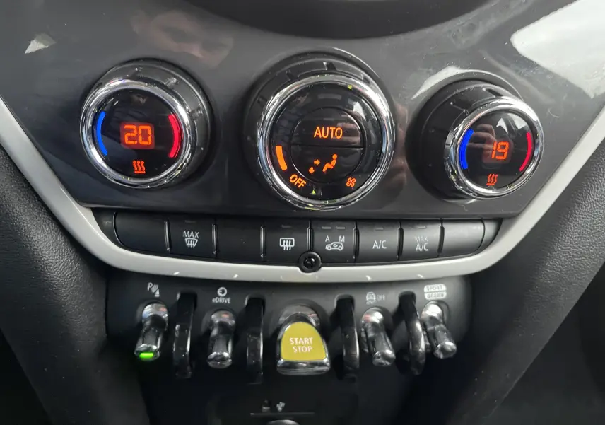 Gros plan sur la console centrale du MINI Countryman bleu, montrant les commandes de climatisation et les interrupteurs chrome.