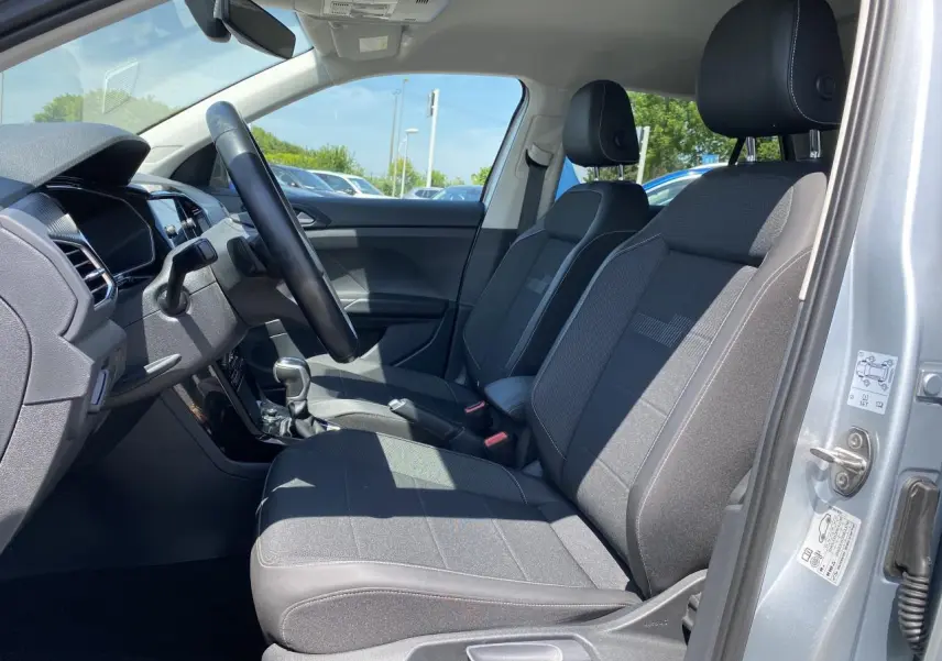 Vue intérieure côté conducteur du Volkswagen T-Cross 2022 argent, montrant sièges avant en tissu gris et tableau de bord moderne.