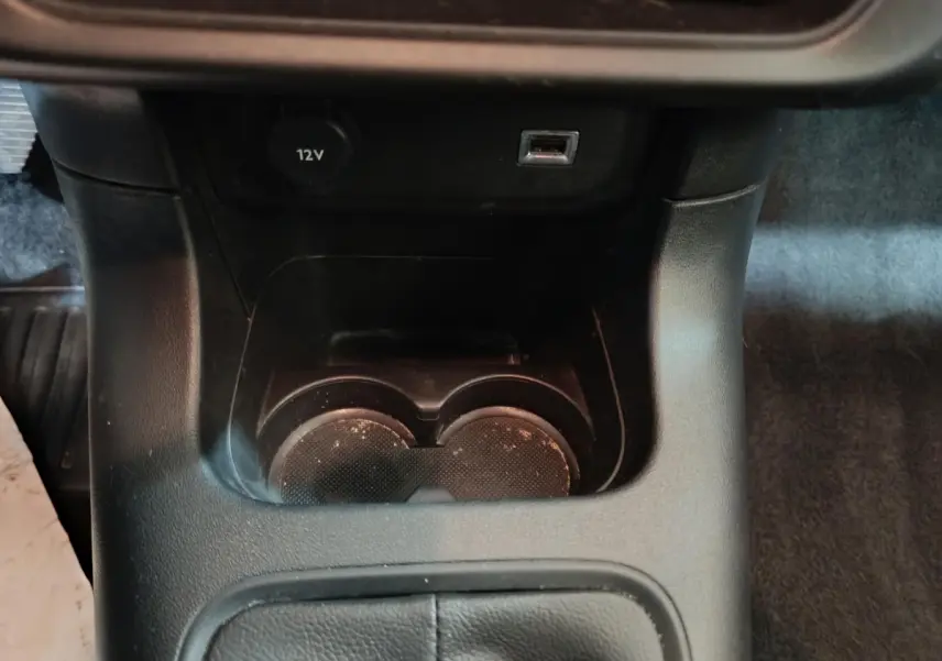 Gros plan sur la console centrale noire de la Citroën C3 2024 avec prise 12V, port USB et porte-gobelets.