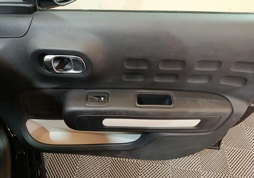 Vue rapprochée de la porte intérieure côté conducteur de la Citroën C3 noire avec poignée argentée et commande de vitre.