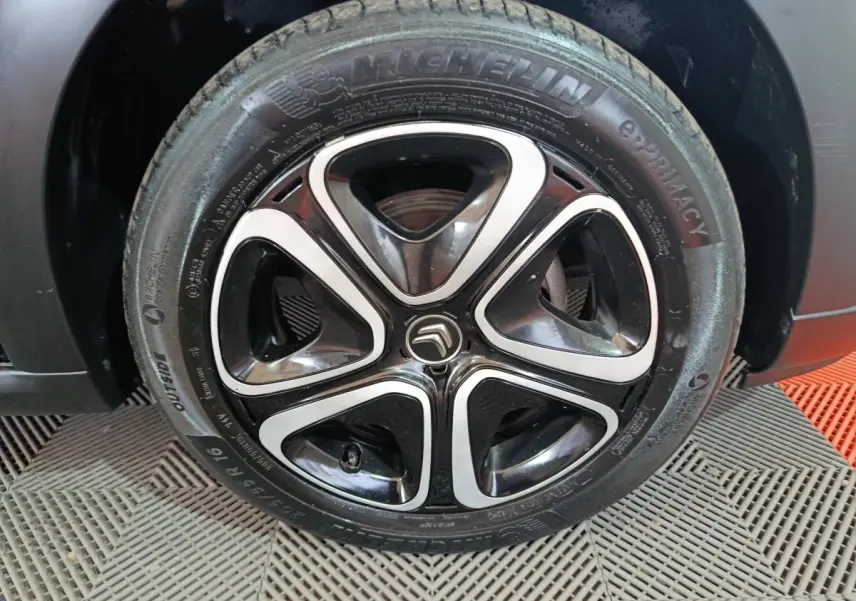 Gros plan sur la jante noire et argentée avec logo Citroën d'une roue Michelin d'une Citroën C3 noire 2024.