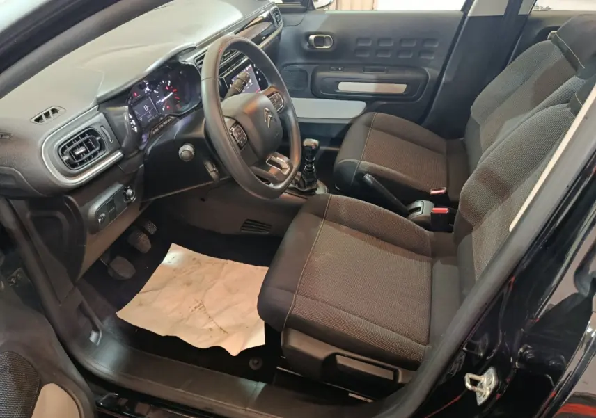 Intérieur avant droit de la Citroën C3 noire 2024, volant multifonctions, tableau de bord digital et sièges tissu gris.