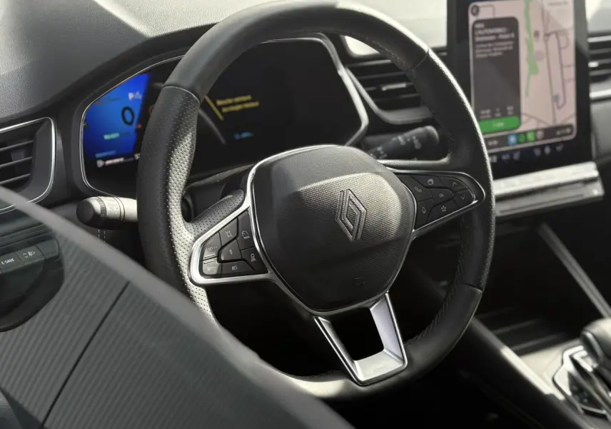 Vue rapprochée du volant noir perforé de la Renault Symbioz 2025 avec écran numérique et système de navigation tactile.