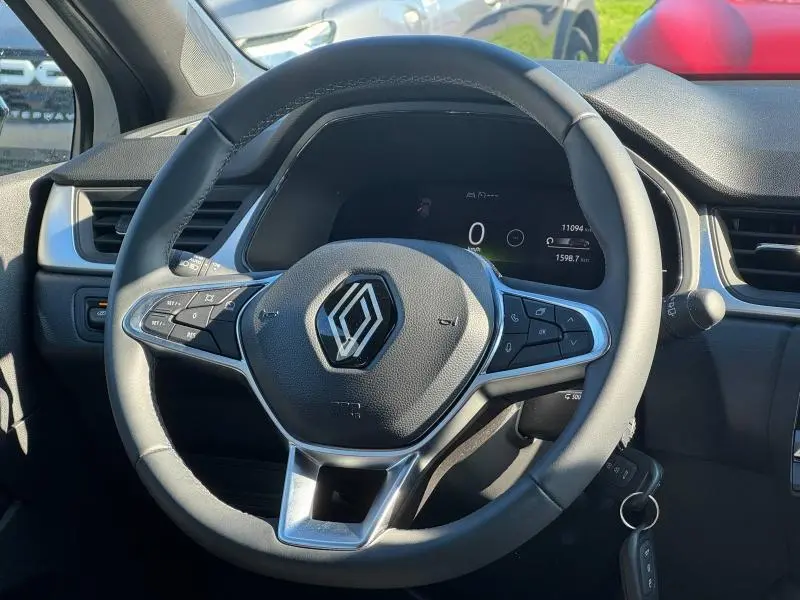 Vue rapprochée du volant du Renault Captur 2025 en peinture blanc nacré, avec commandes intégrées et tableau de bord numérique.