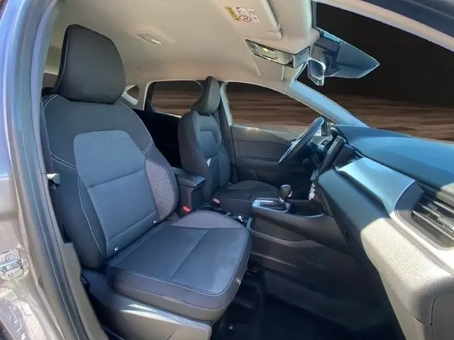 Vue intérieure côté conducteur de la Renault Captur gris clair 2023, sièges tissu noir et tableau de bord moderne.