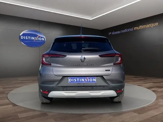 Vue arrière d'un Renault Captur gris clair 2023, avec feux LED et logo distinctif sur fond showroom.