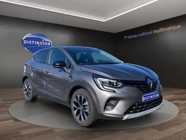 Vue 3/4 avant d'un Renault Captur gris clair 2023 avec phares LED et jantes alliage distinctives dans un showroom.