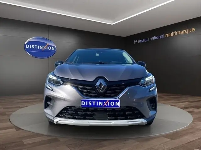 Vue frontale d'un Renault Captur gris clair 2023 avec calandre noire et phares LED allumés en showroom.