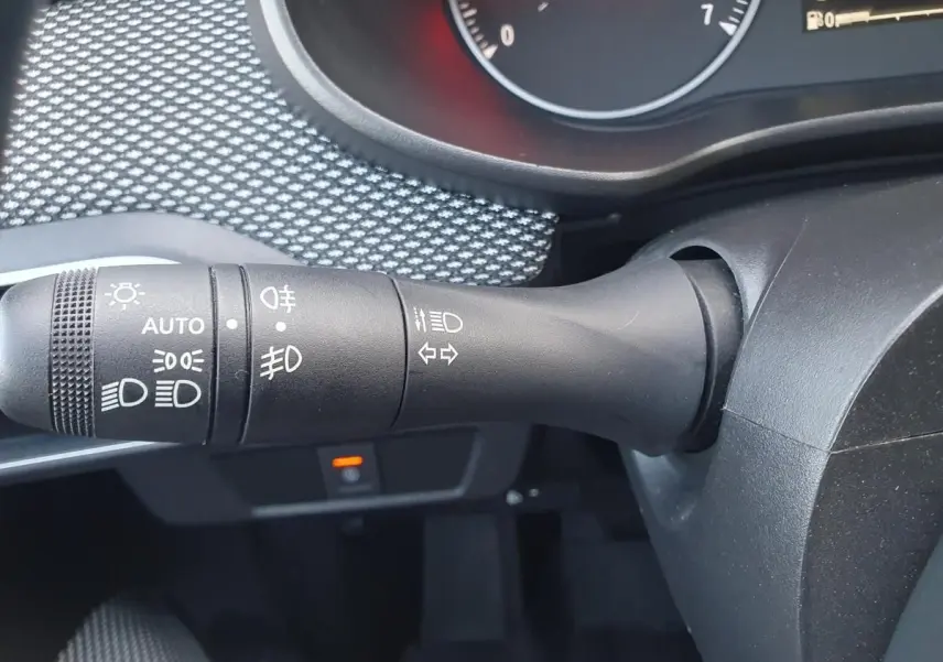 Gros plan sur la commande des feux et clignotants côté gauche du volant dans un intérieur gris d'une Dacia Sandero 2024.
