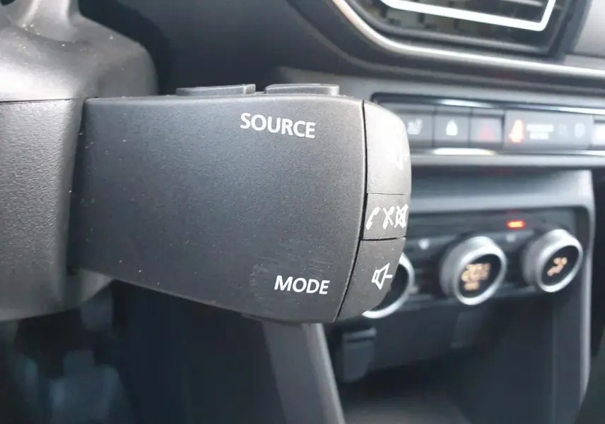 Gros plan sur la commande au volant du DACIA Sandero 2024, mettant en valeur les boutons source et mode audio.