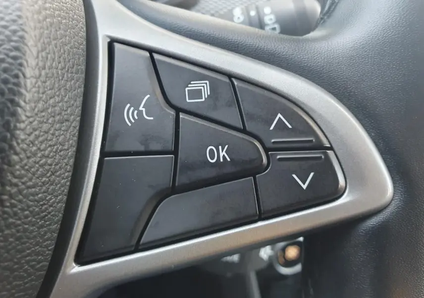 Gros plan sur les commandes multifonctions noires du volant gris d’une Dacia Sandero 2024, boutons OK et flèches visibles.