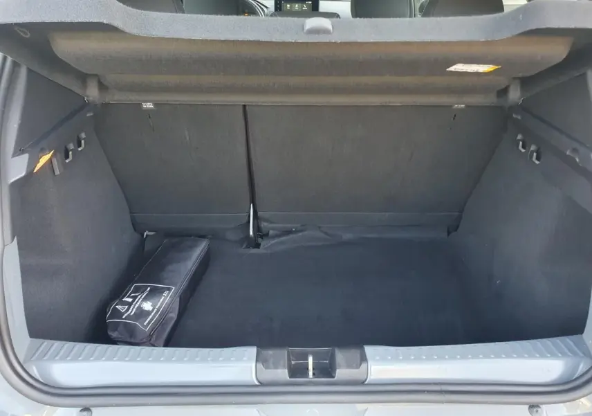 Coffre ouvert vu de l'arrière d'une Dacia Sandero gris urbain 2024, avec un kit de secours noir posé à gauche.