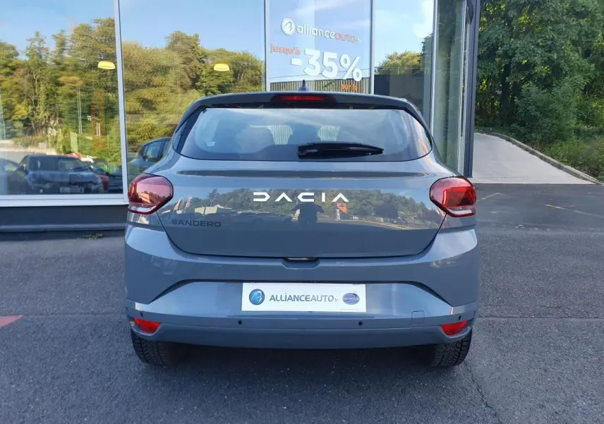 Vue arrière d'une Dacia Sandero 2024 gris urbain avec feux arrière rouges et logo DACIA visible.