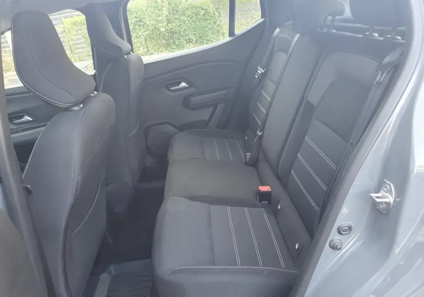 Vue intérieure arrière côté droit de la Dacia Sandero 2024 gris urbain, montrant les sièges arrière en tissu noir avec surpiqûres blanches.