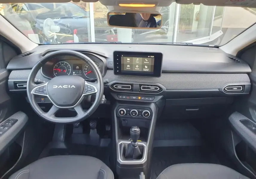 Vue intérieure avant du tableau de bord et volant DACIA Sandero 2024 avec écran tactile et boîte manuelle.