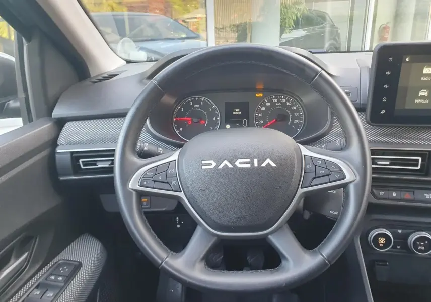 Vue rapprochée du volant multifonction noir de la Dacia Sandero 2024 avec tableau de bord et écran tactile.