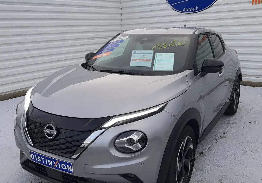 Nissan Juke 1.6 HEV gris perle métal en 3/4 avant droit, avec calandre noire et jantes bi-ton visibles.