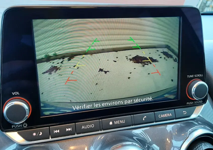 Écran central du Nissan Juke 2024 gris perle métal montrant l'image de la caméra de recul avec repères colorés.