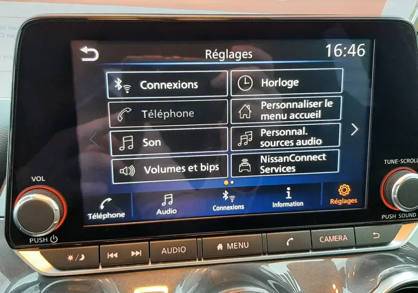 Écran tactile central du Nissan Juke 2024 gris perle, affichant le menu Réglages avec options de connexion et audio.