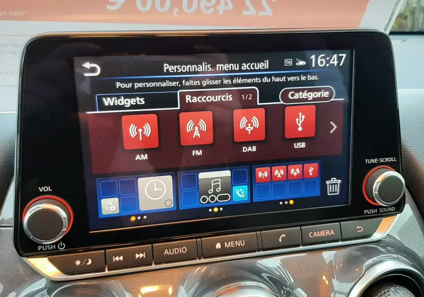 Écran tactile central du Nissan Juke 2024 avec commandes audio et climatisation, intérieur gris perle métal.
