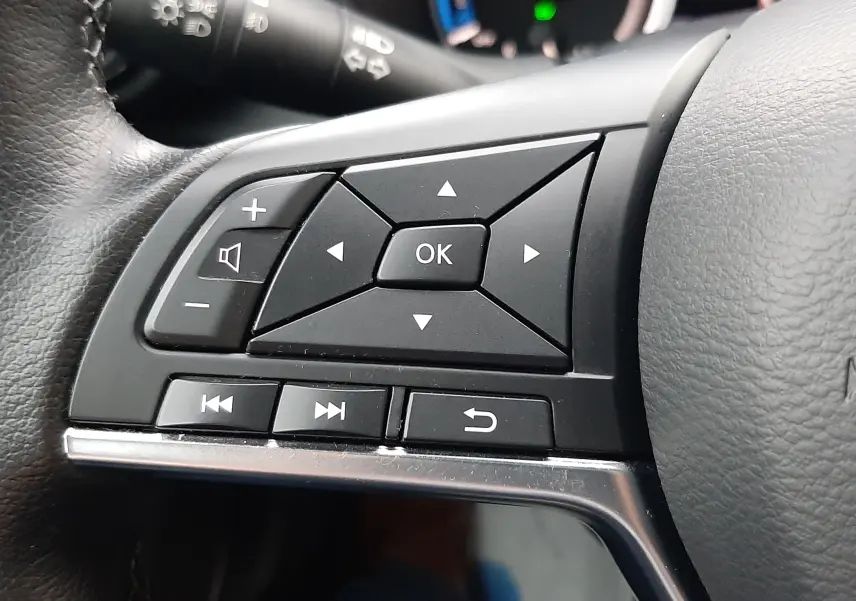 Gros plan sur les commandes multifonctions à gauche du volant du Nissan Juke gris perle 2024, affichage hybride en arrière-plan.