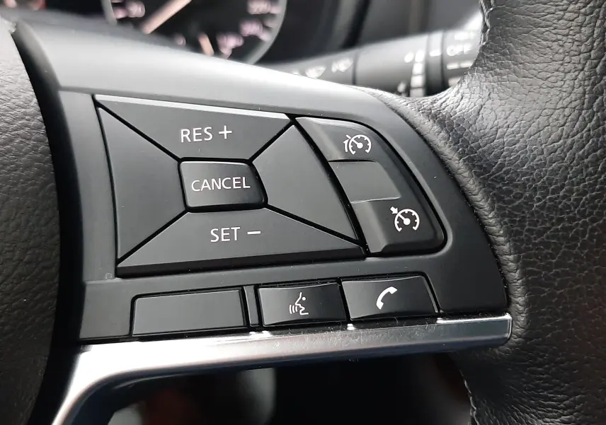 Gros plan sur les commandes de régulateur de vitesse et téléphone au volant cuir noir du Nissan Juke gris perle 2024.