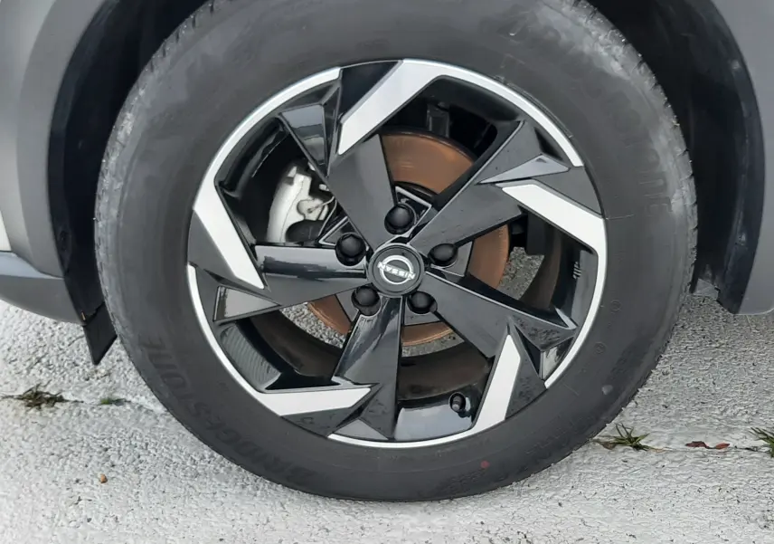 Gros plan sur la roue avant droite d'un Nissan Juke gris perle métal avec jante noire et argentée au design anguleux.